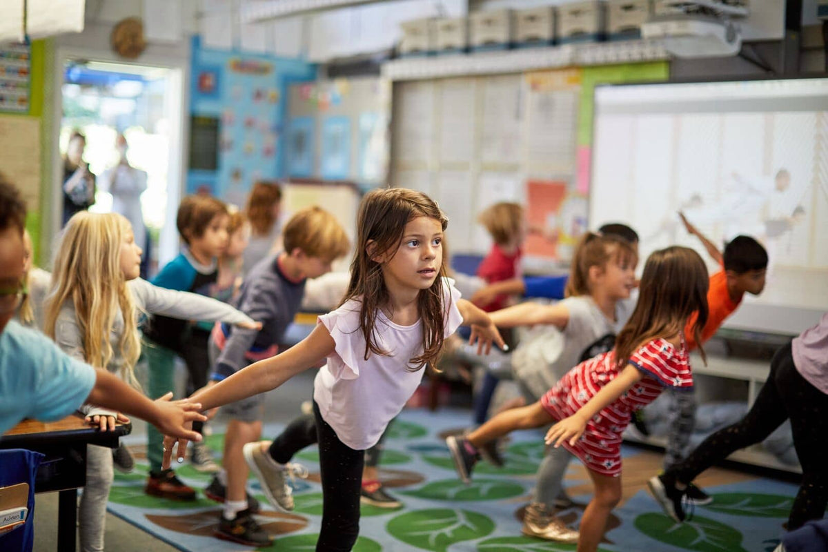 Children practicing yoga in a classroom on a communal carpet area.